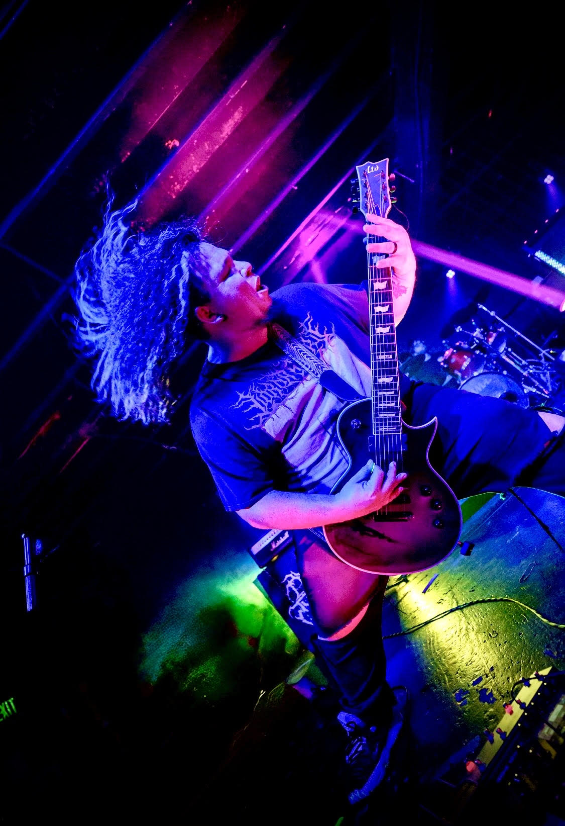 Person with curly hair playing an acoustic guitar on stage with colorful lights and fog effects.