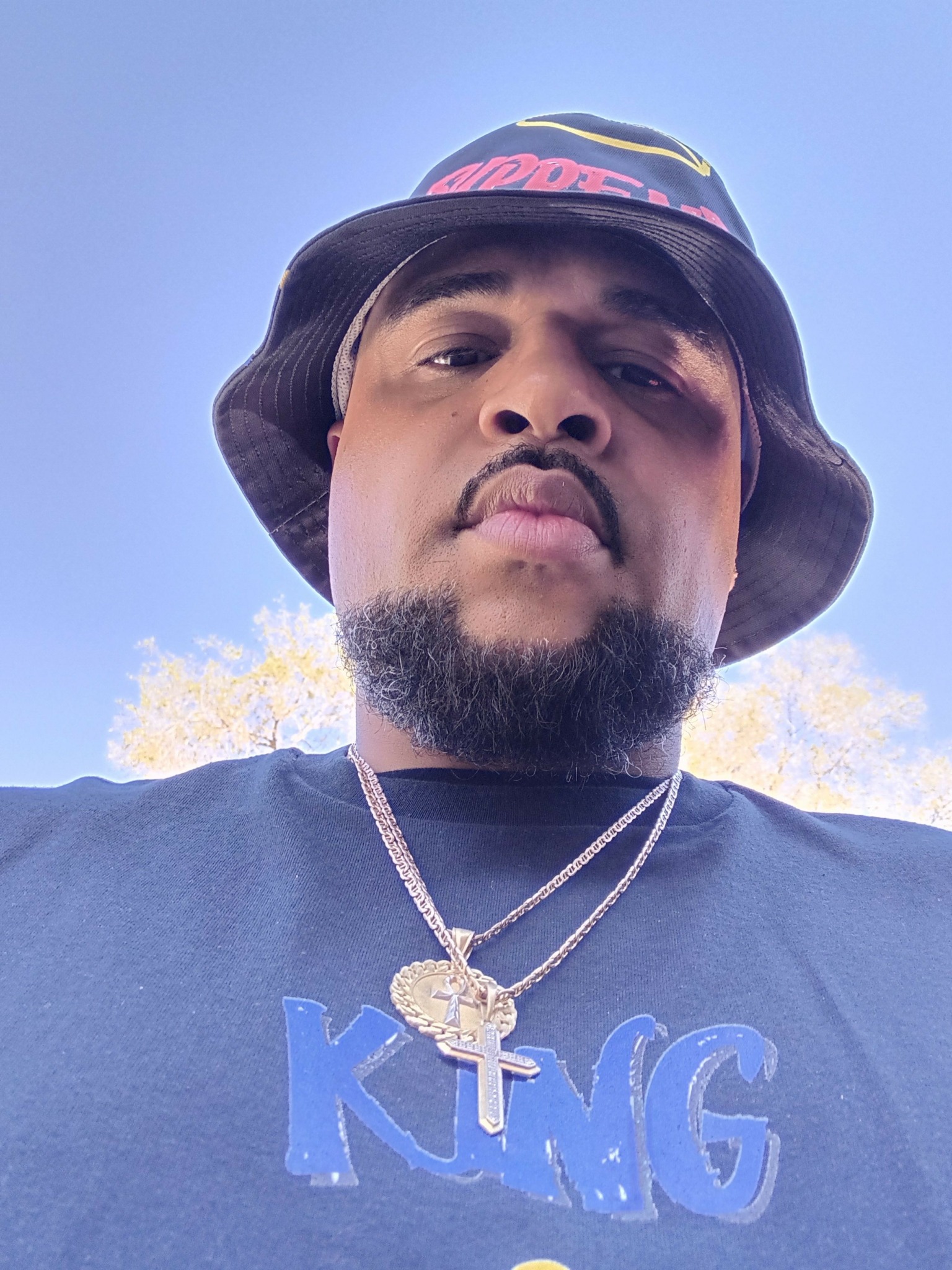 Man wearing a black hat and shirt outdoors with a clear blue sky background.