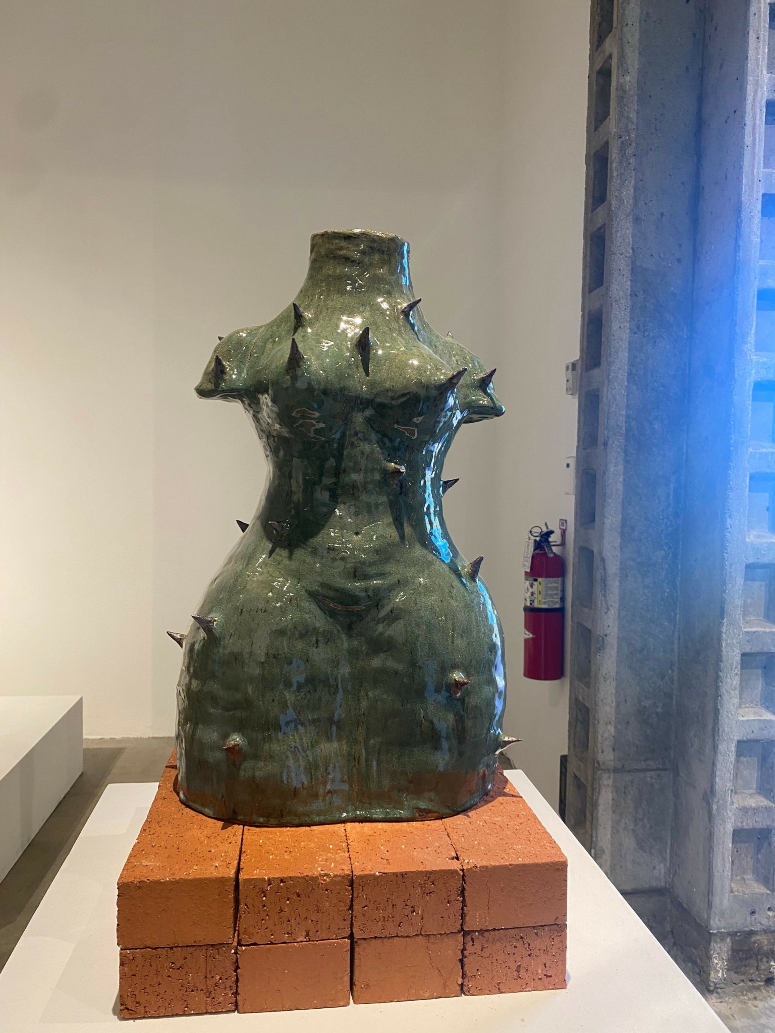 A sculpture of a wolf's head on a rounded base, placed on a brick platform, with a building in the background.