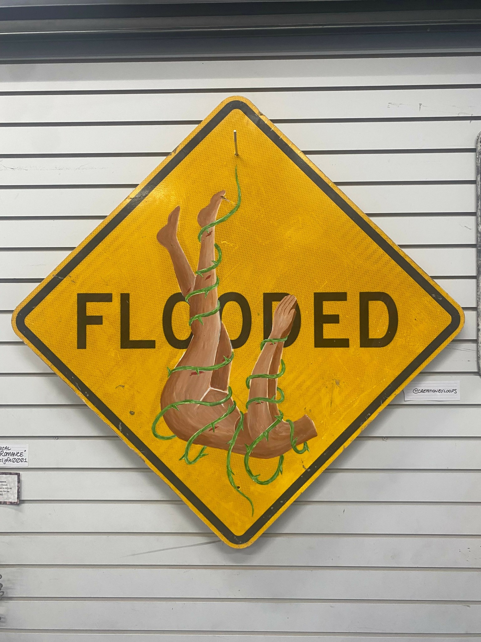 Flooded road sign with a dog illustration, yellow diamond shape, mounted on a wall.