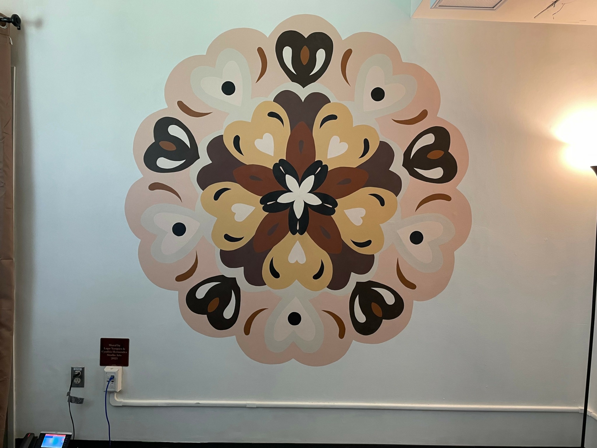 Decorative circular wall art with symmetrical floral pattern in beige, black, and white colors, on a light blue wall.