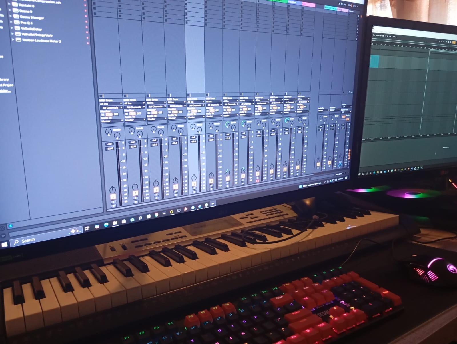 Music production setup with a computer screen displaying digital audio workstation software, a keyboard, and a colorful keyboard in front.