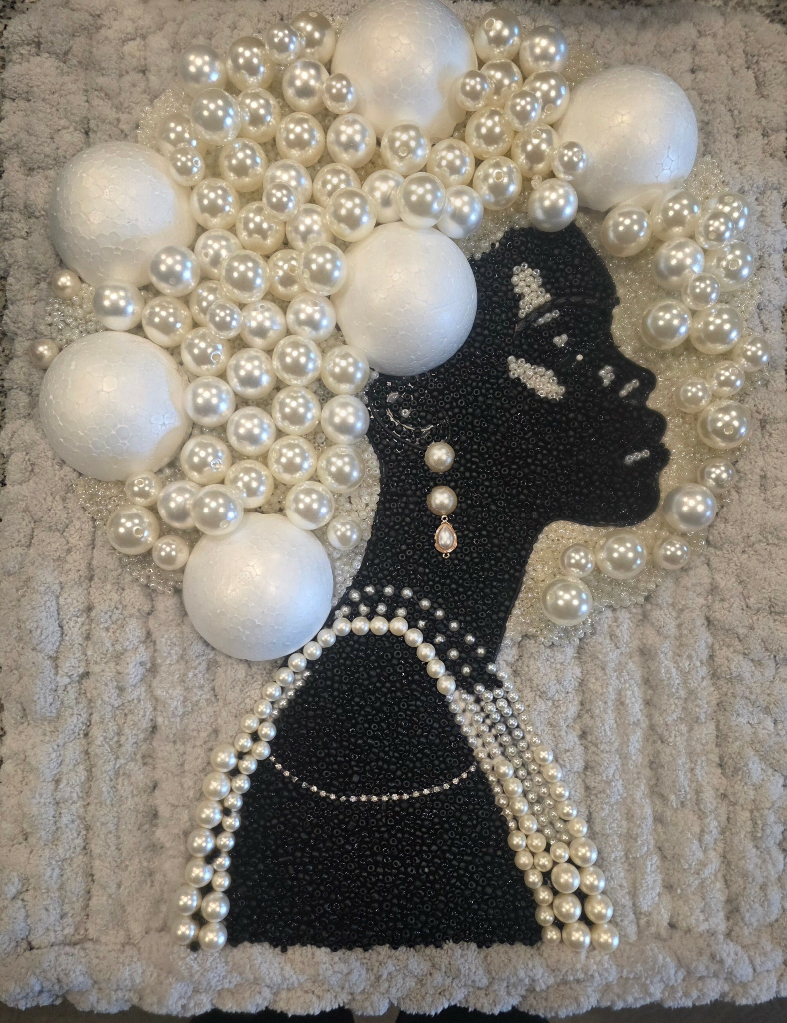 Silhouette of a woman with pearl jewelry and large pearl headpiece, made from beads and pearls on textured background.