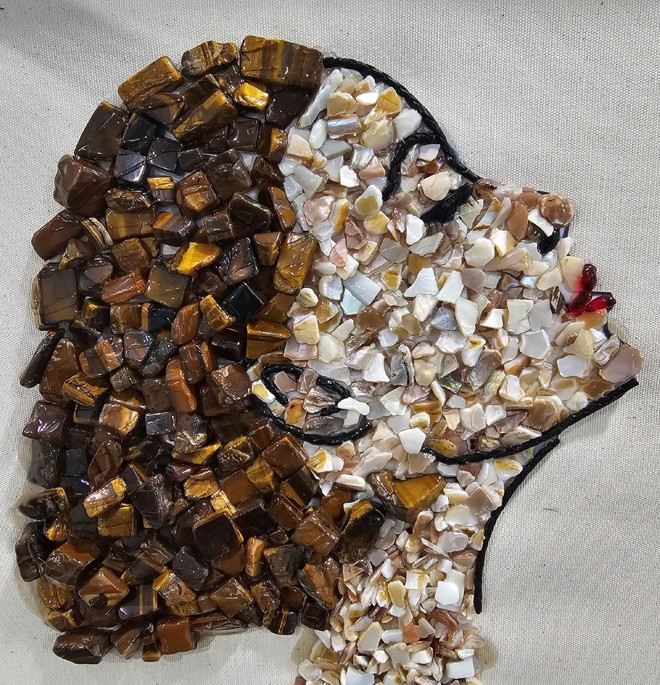 Mosaic artwork of a woman's face made with small stones, with dark hair and light skin, on a light background.