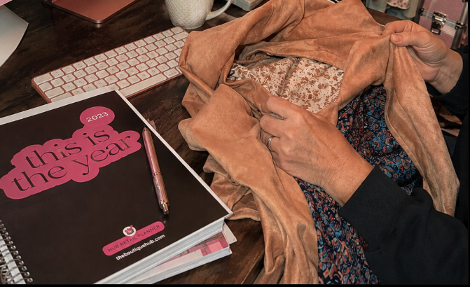 Person sewing fabric with a book titled 'This is the year' and a pen on a wooden table.