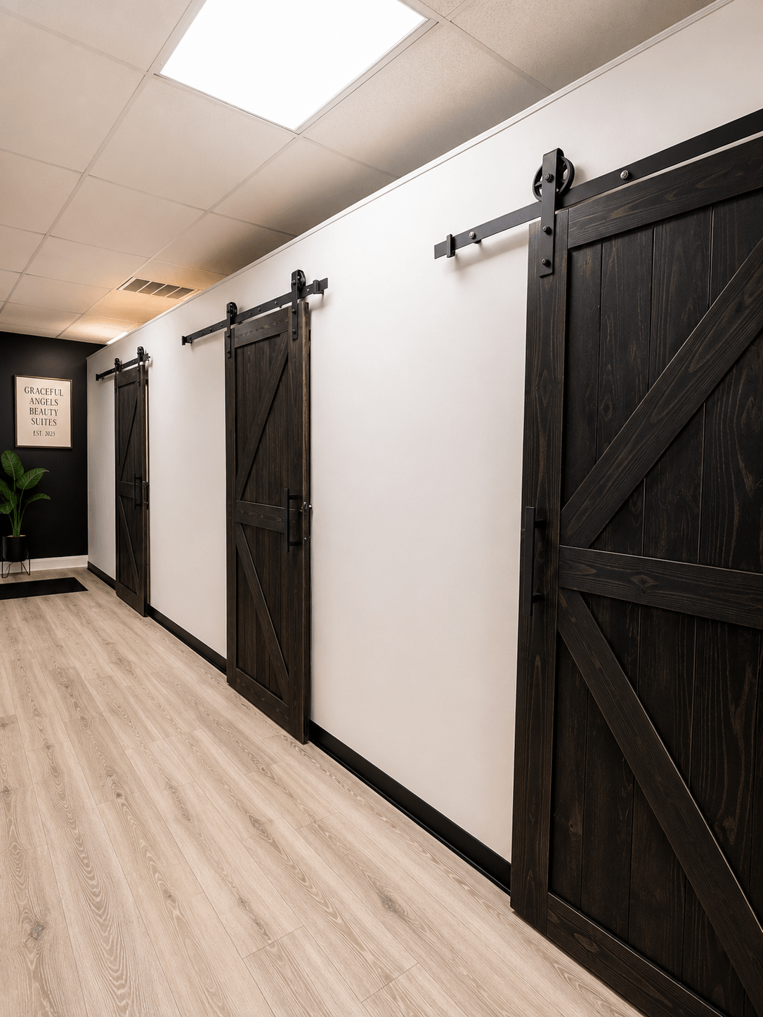 Three black sliding barn doors on a white wall in a hallway with light wood flooring.