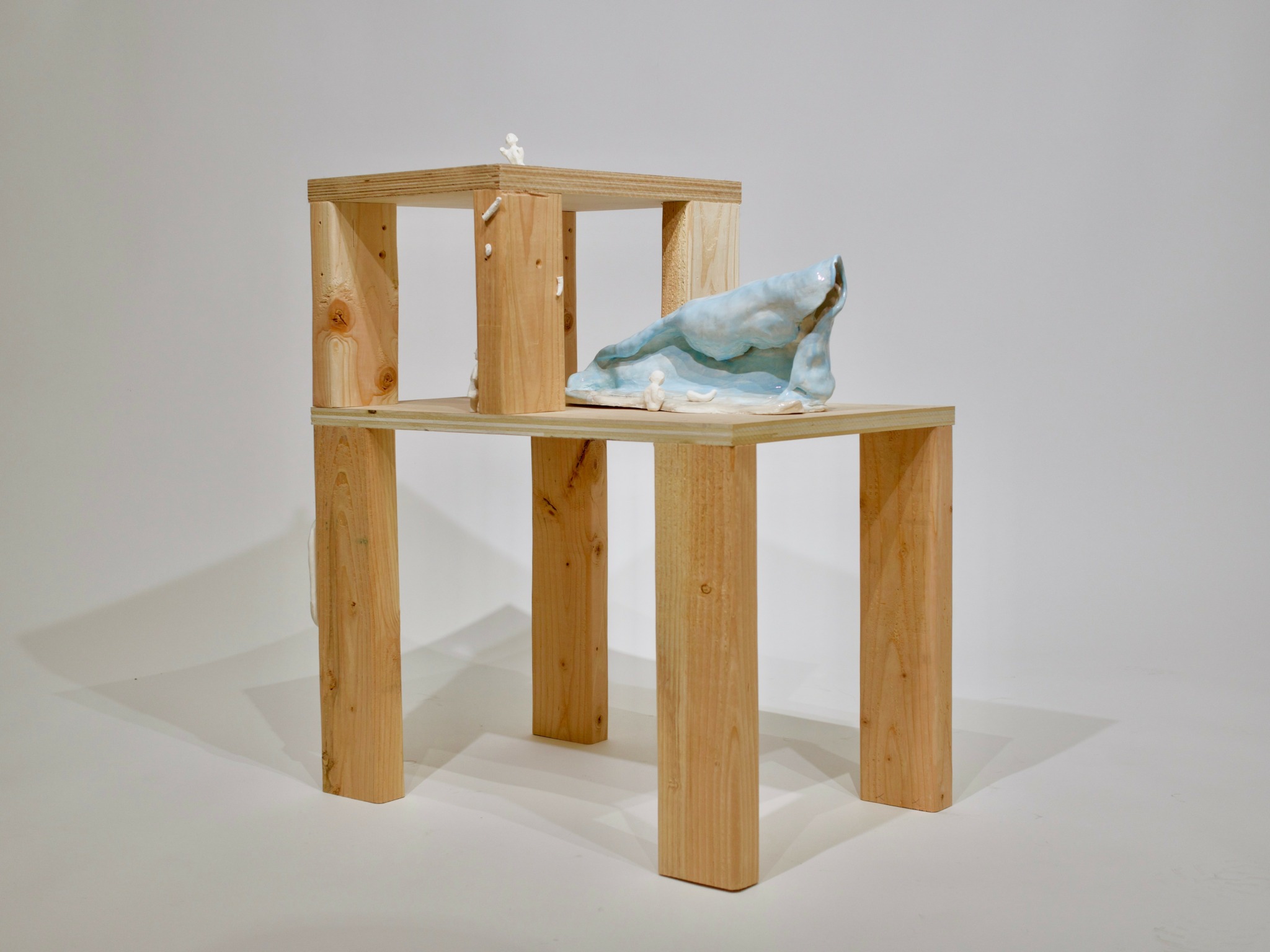 Wooden display stand with a ceramic whale figurine on top, against a plain background.