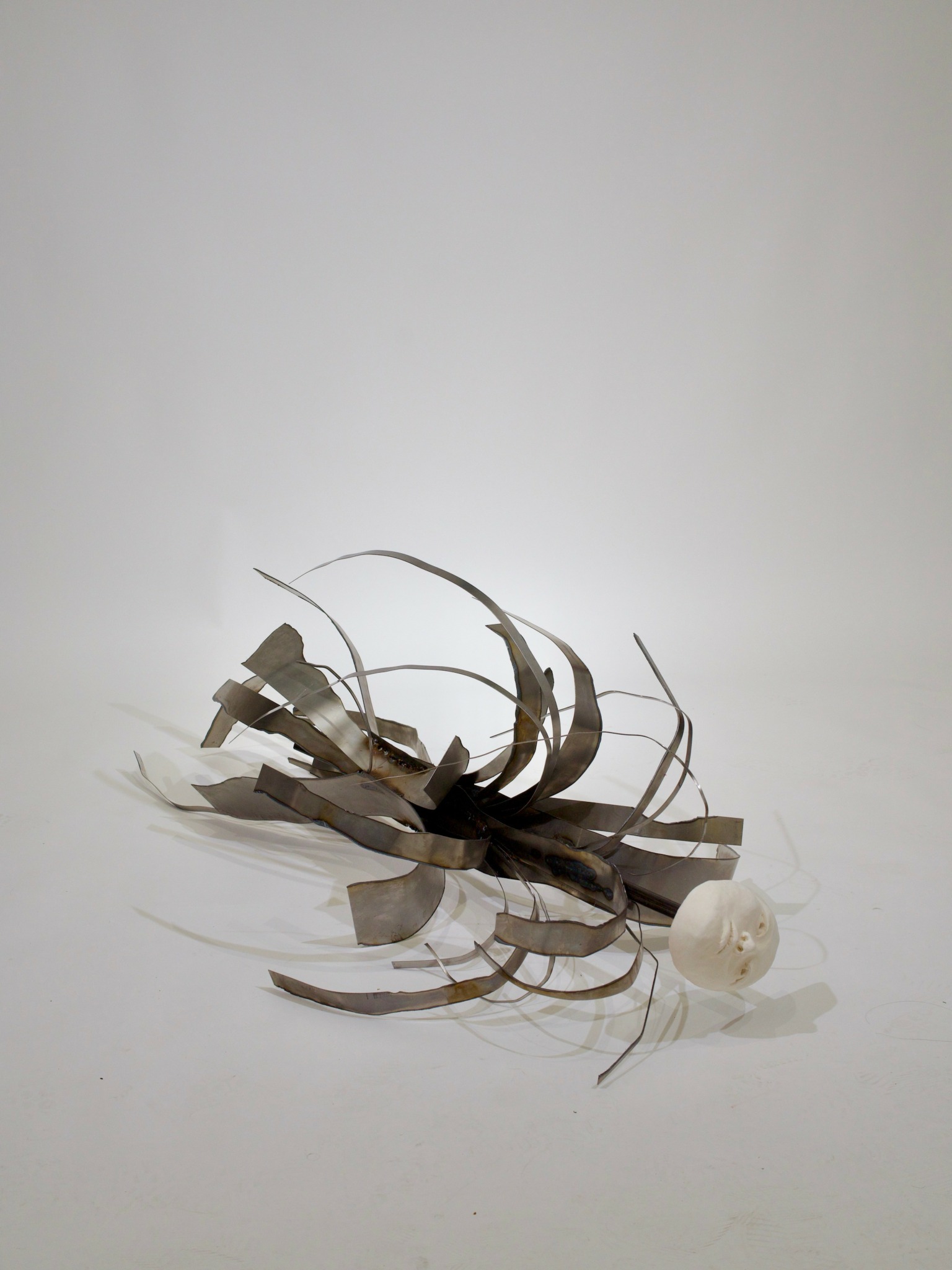 Abstract sculpture with curved metallic and plastic elements on a white background.