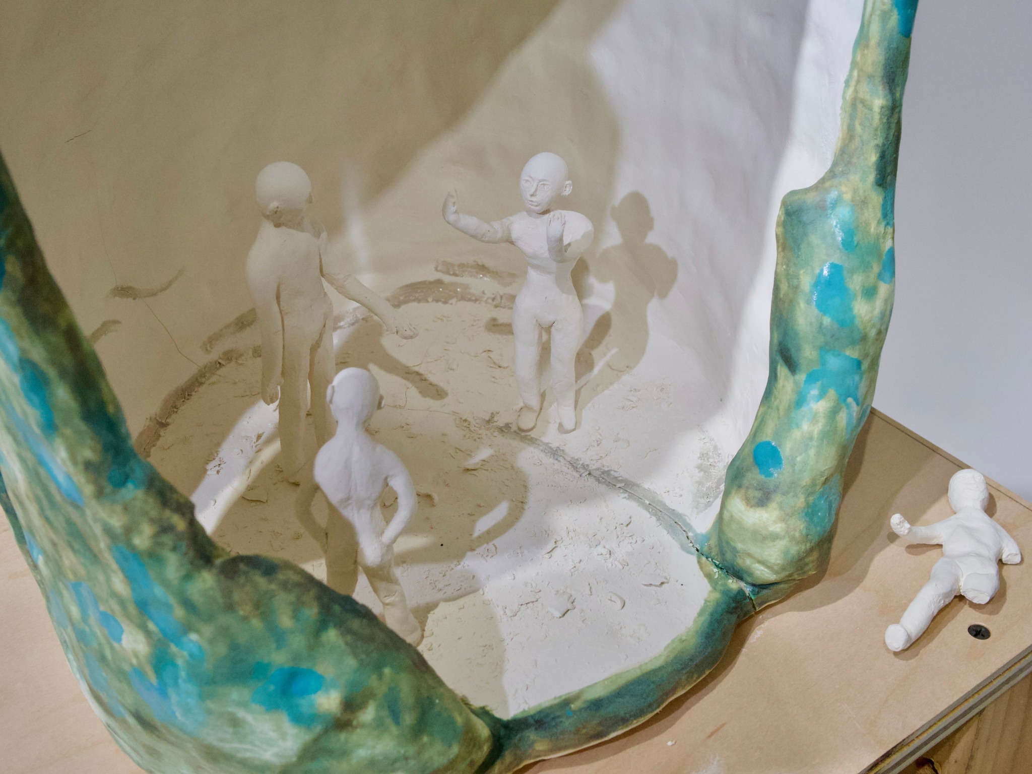 Four small white figurines inside a glass container with a painted rim, some lying outside on a surface.