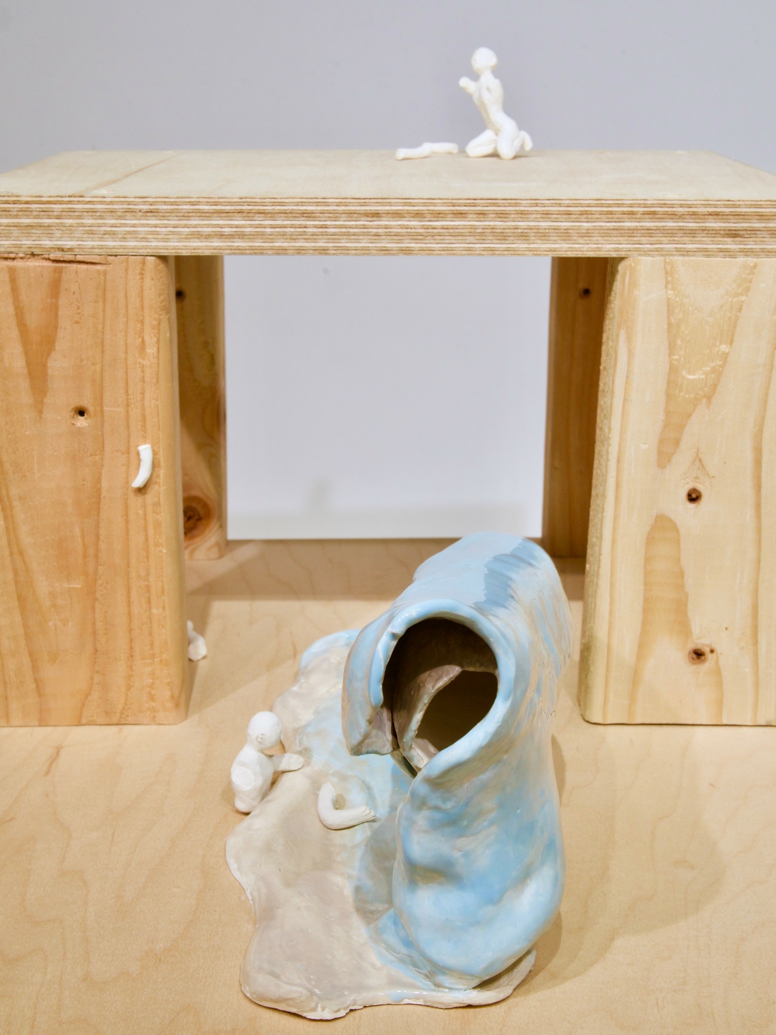 A small figurine on a wooden table, a ceramic sculpture with a hole, and wooden blocks in the background.