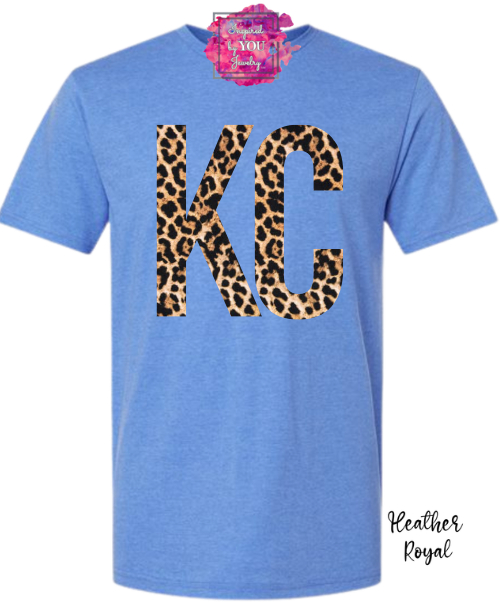 Blue T-shirt with large leopard print letters 'KC' on front, short sleeves, and a pink tag at the collar.