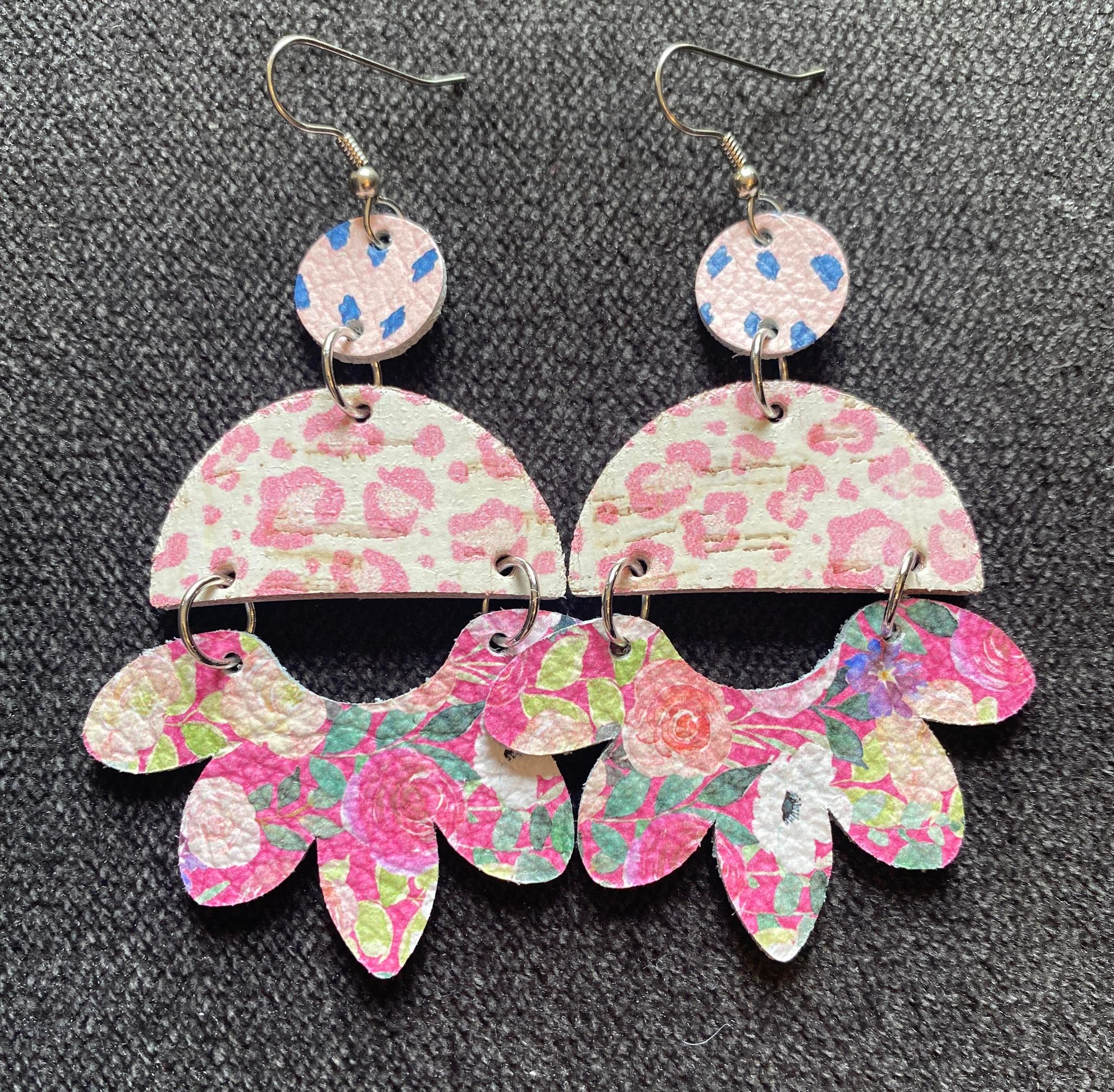 Pair of colorful, patterned earrings with semi-circular and leaf-shaped elements on a dark background.