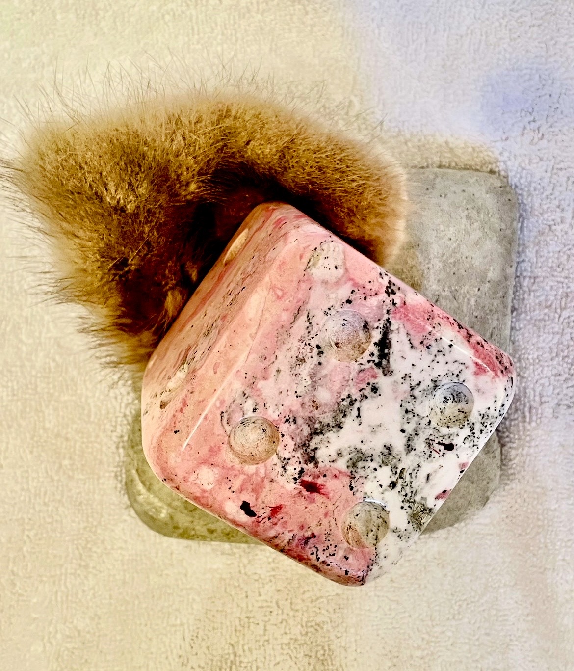 A pink and black marbled soap with a fluffy brown brush on a light surface.