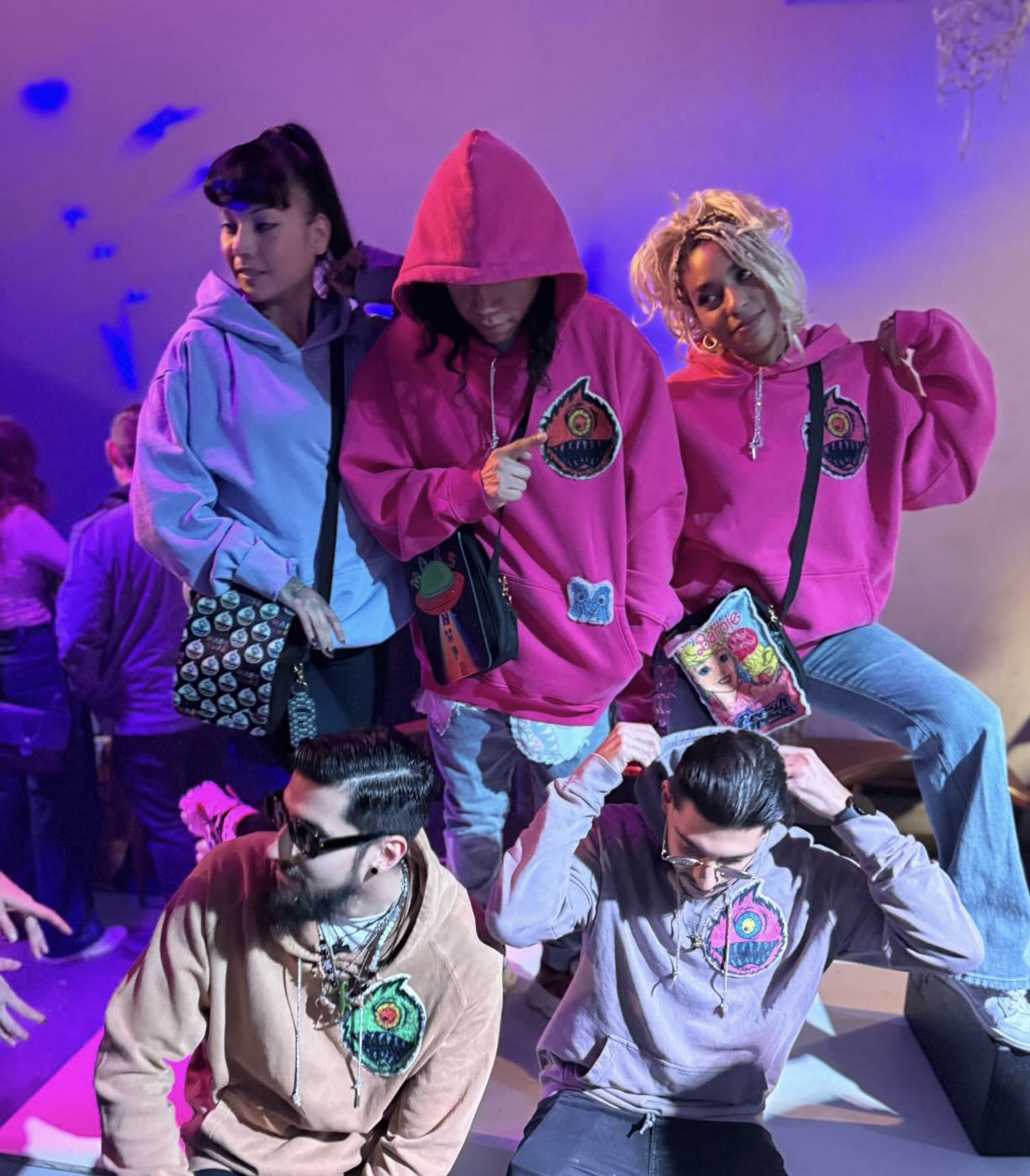 Group of five young people in colorful hoodies, some sitting and some standing, in a vibrant indoor setting.